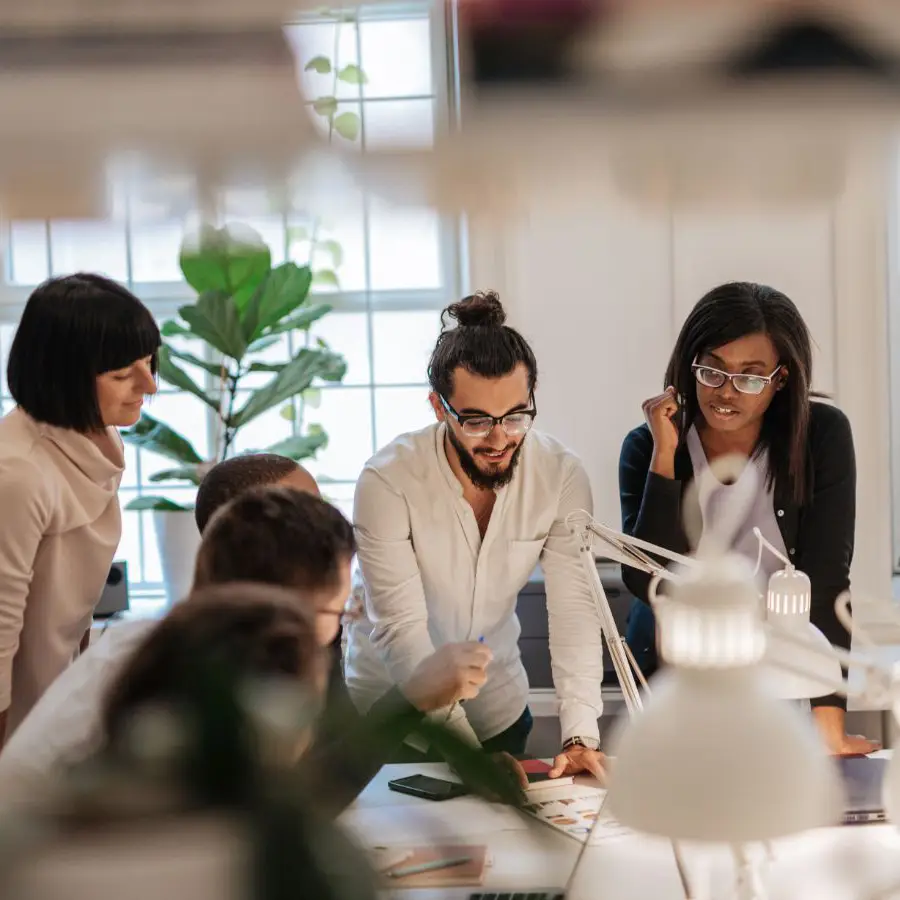 Équipe professionnelle collaborant autour d'une table dans un bureau moderne, avec un environnement lumineux et des plantes en arrière-plan.
